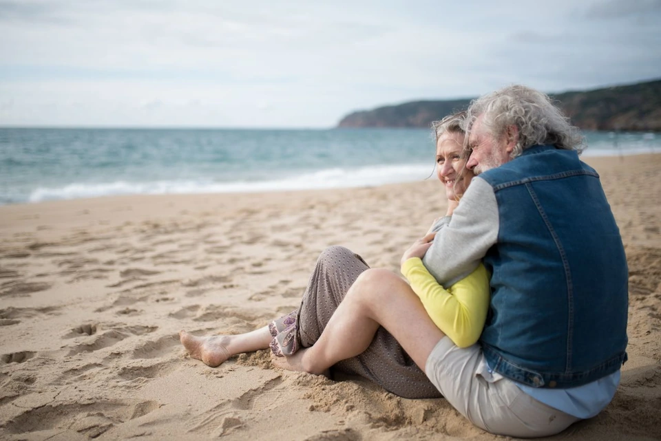 An older couple sitting together on a beach.