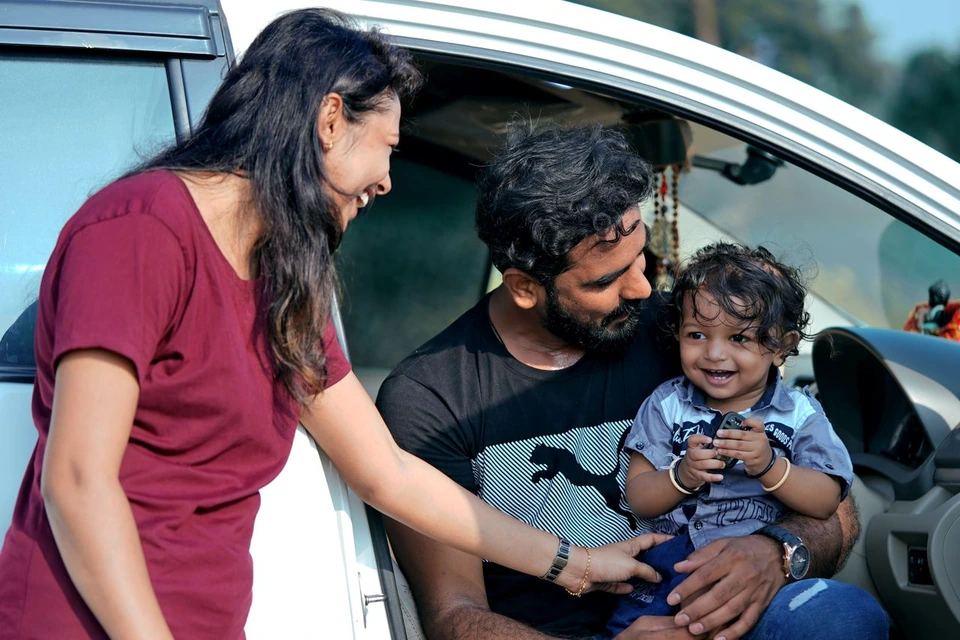 Parents and their child sharing a moment beside a car.