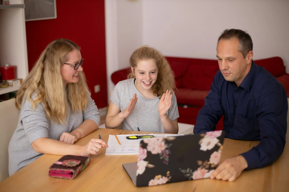 Parents helping their child at a table at home.