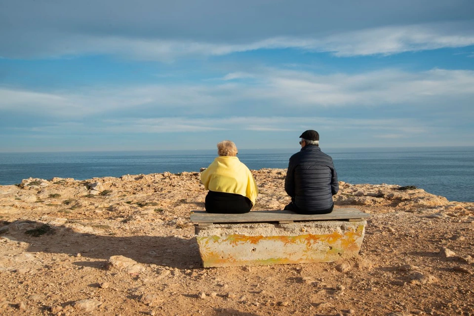 A couple sitting on a bench looking out to sea.