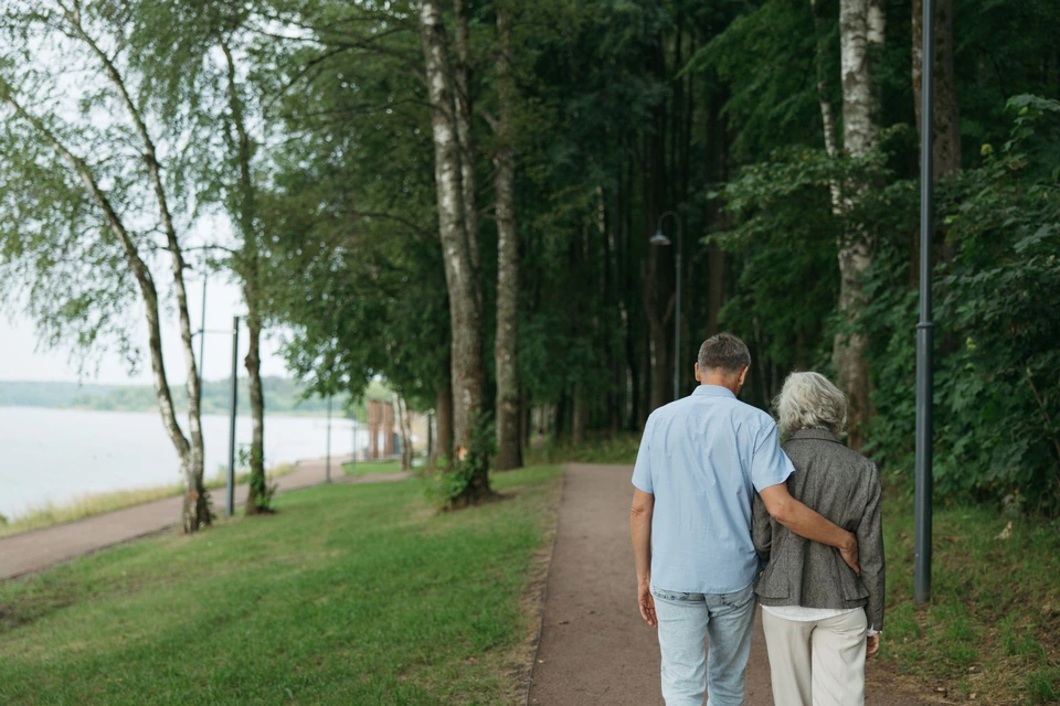 A couple walking arm in arm beside a lake.